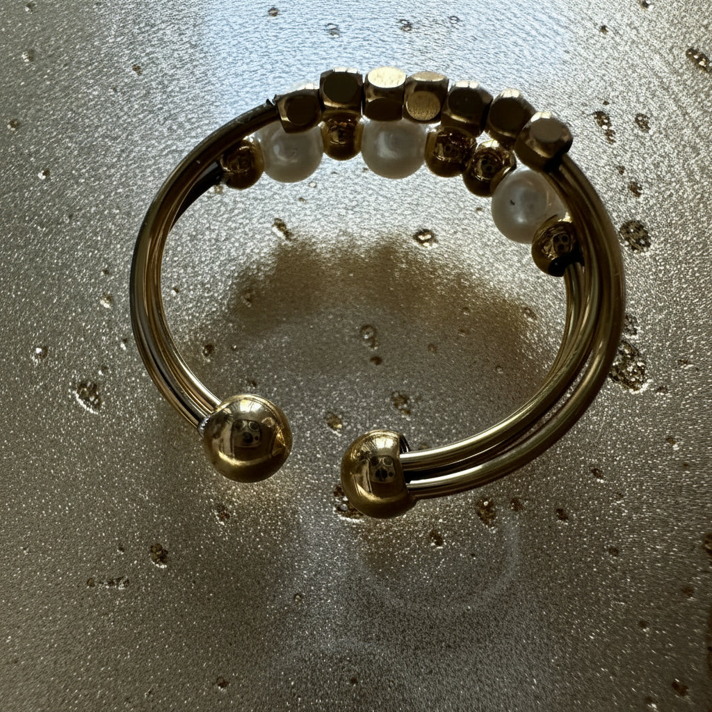 A gold-toned open cuff ring with white pearl-like beads and small metallic accents